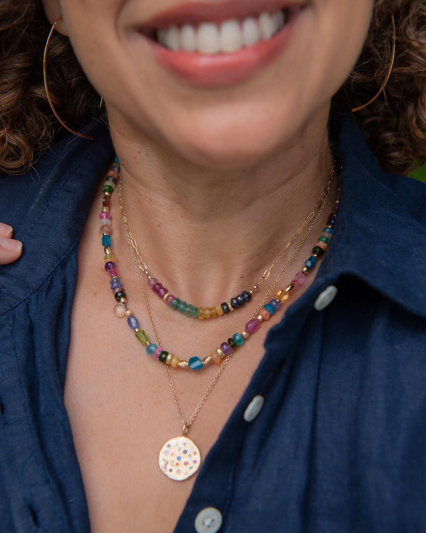 Close-up of a person wearing colorful beaded gemstone necklaces and a blue shirt.